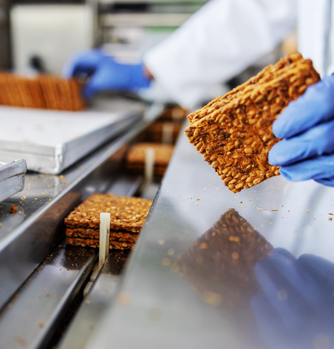 Quality technician in blue gloves inspecting a baked oat product on the line