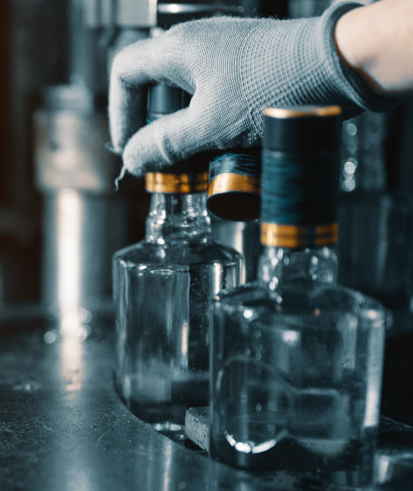 Gloved hand capping glass spirit bottles on a bottling line
